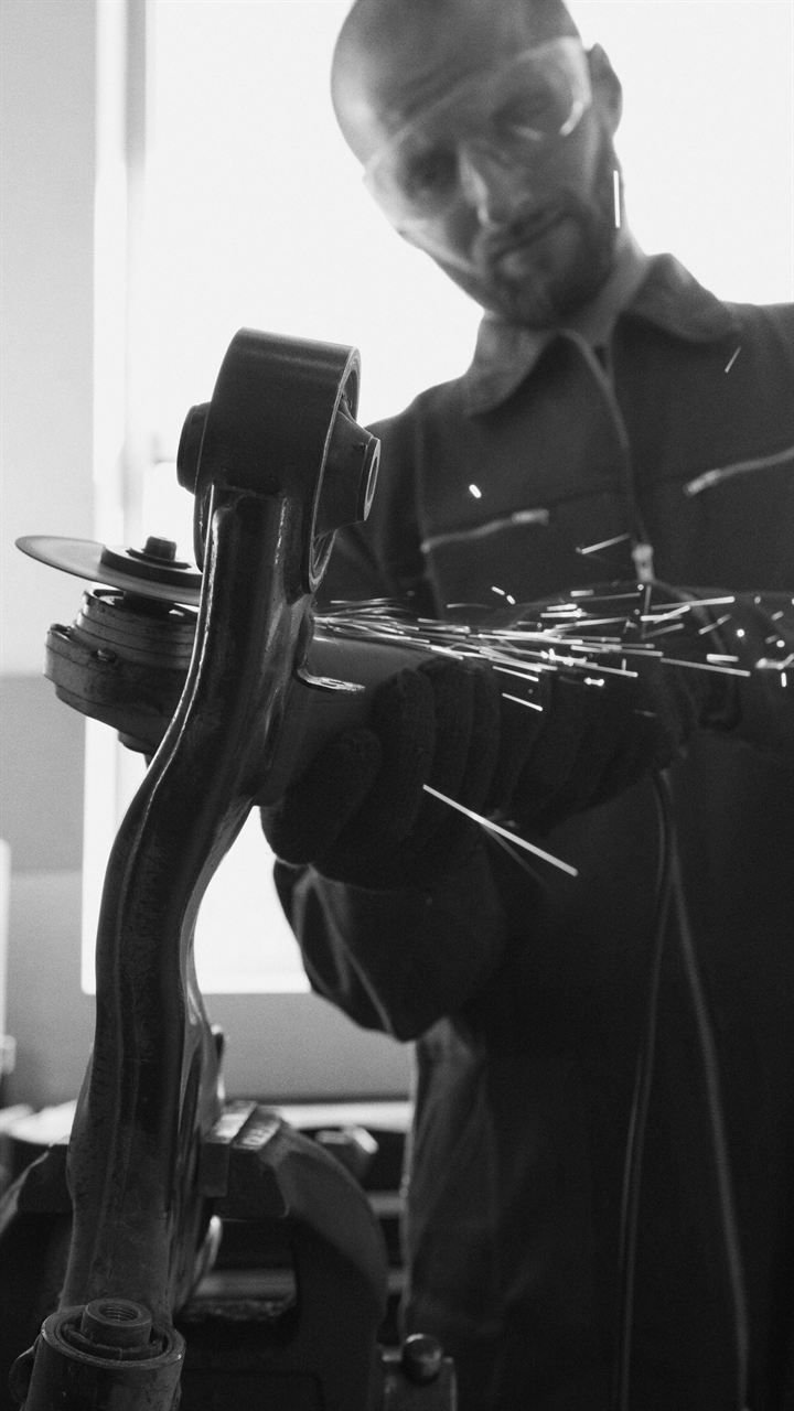 Mecánico con gafas de protección sujetando una pieza de suspensión, en blanco y negro
