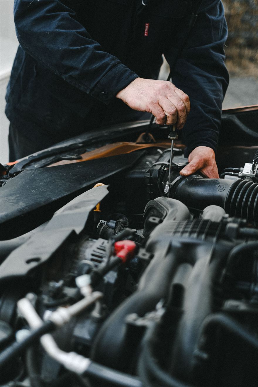 Manos de un mecánico trabajando en el motor de un coche con el capó abierto