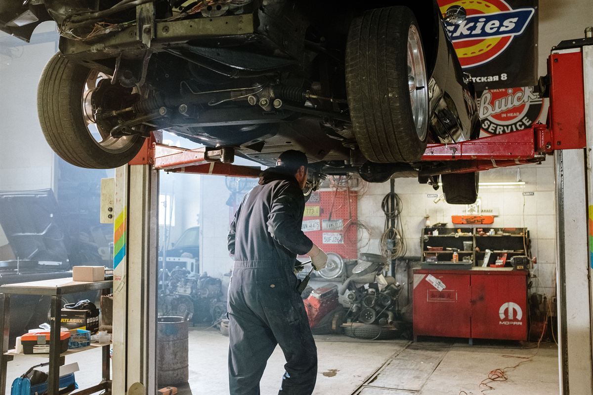 Mecánico revisando los bajos de un coche elevado en el taller